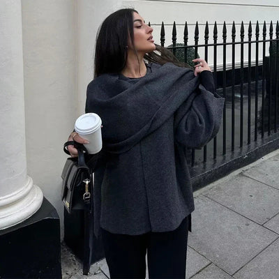 Frau in einer dunkelgrauen Jacke mit breitem, über die Schultern gelegtem Kragen und schwarzer Handtasche.