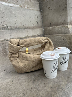 Beigefarbene geflochtene Handtasche mit Knotenhenkel auf einer Betontreppe