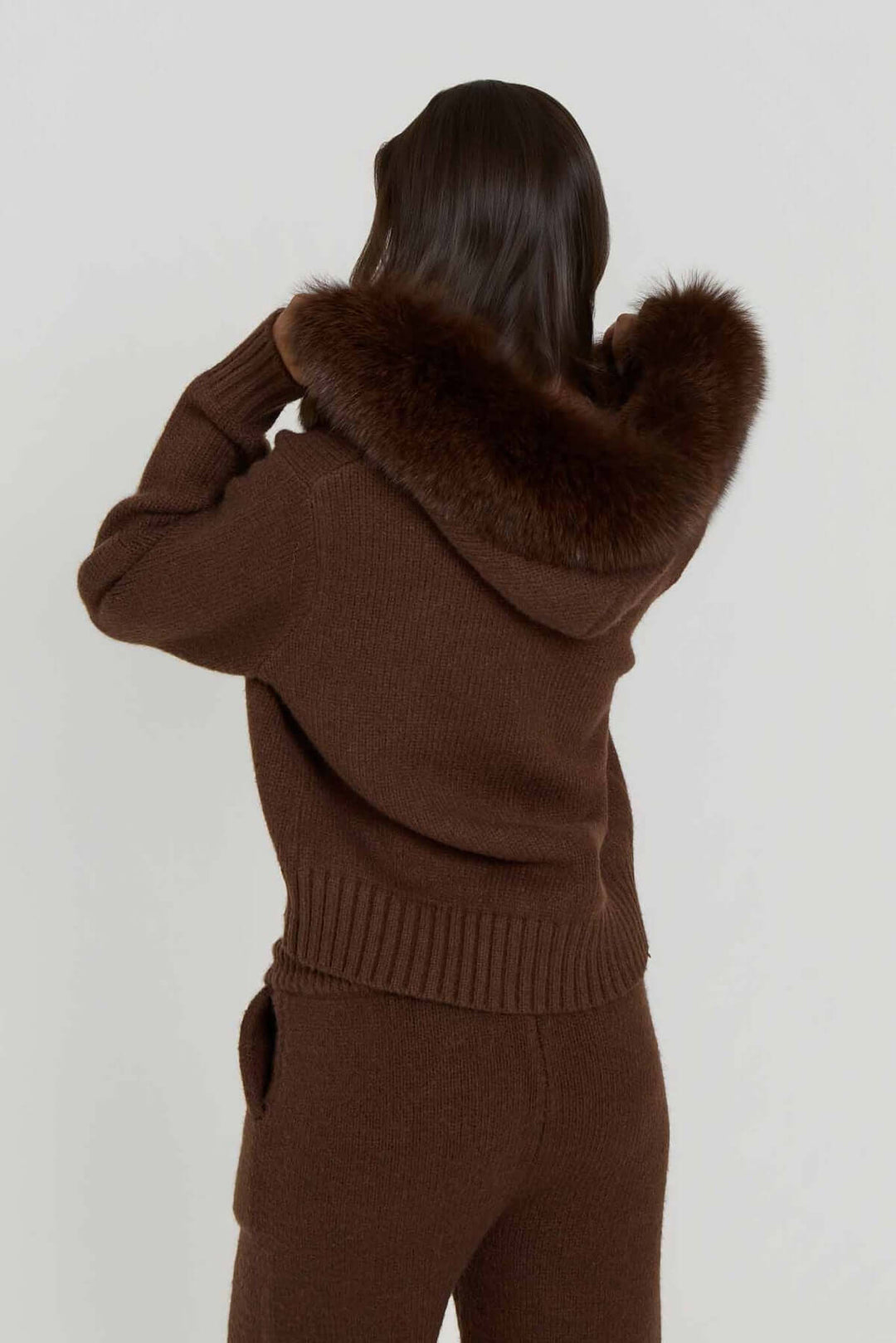 Frau mit braunem Pullover und Kunstpelzkapuze im SOFIA – 2‑Teiler Set von Miraee Paris.