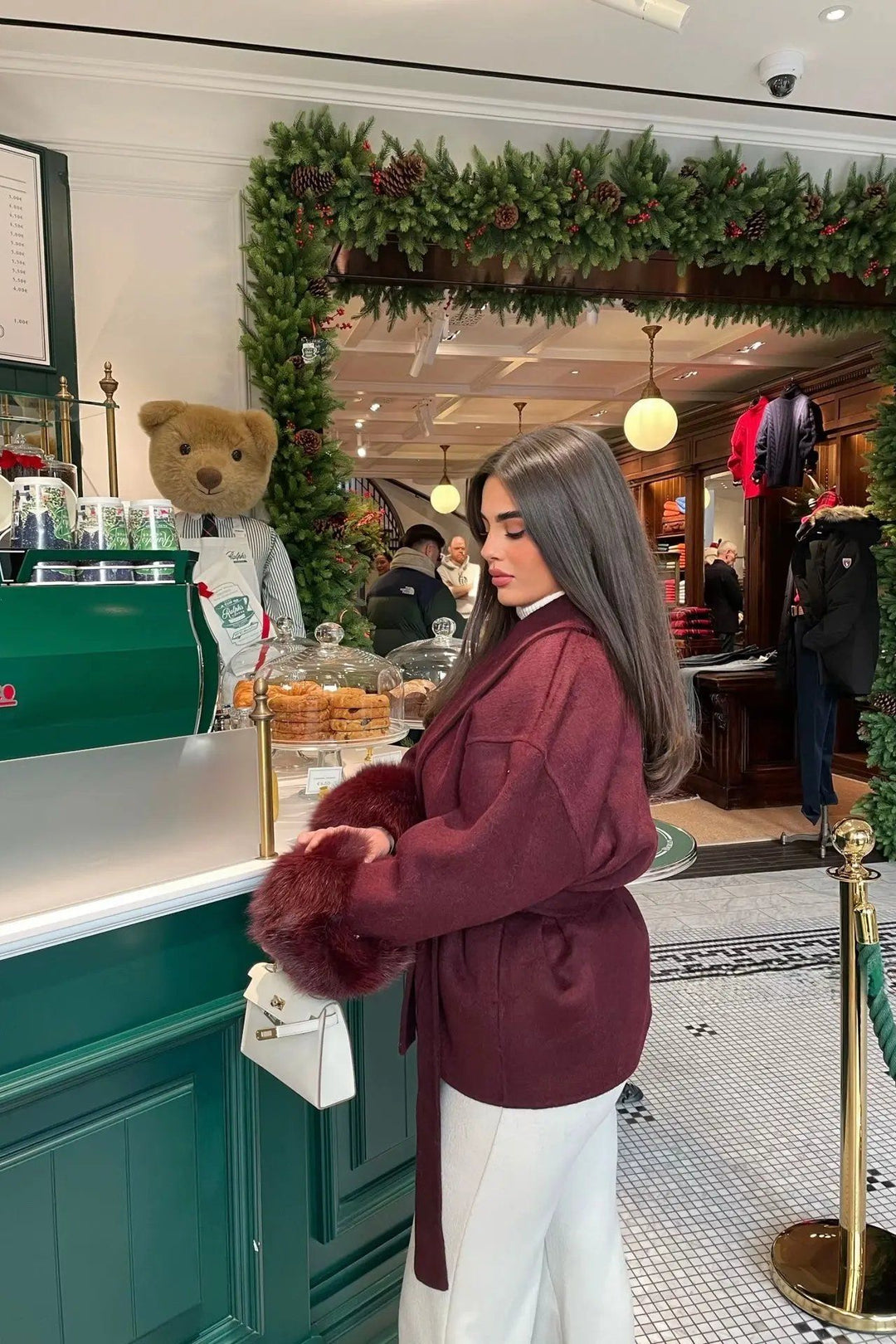 ARCTIC GRACE – Eleganter Wollmantel für Damen in einem eleganten Café-Umfeld mit Weihnachtsdeko.