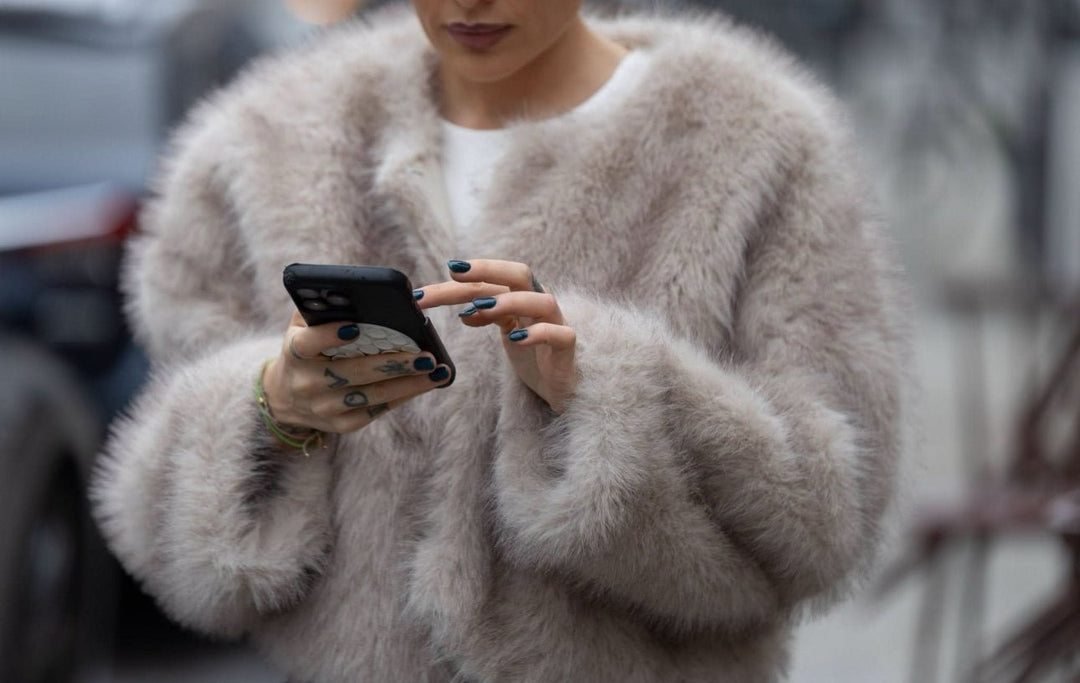 DIVINE – Luxuriöse Kunstpelzjacke mit Eleganzfaktor, getragen von einer Frau, während sie ihr Handy benutzt.