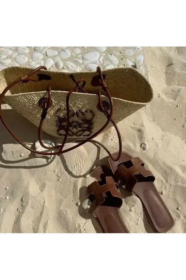 Luna Cut Ledersandale und elegante Tasche auf dem Sand am Strand, perfekt für Sommertage.