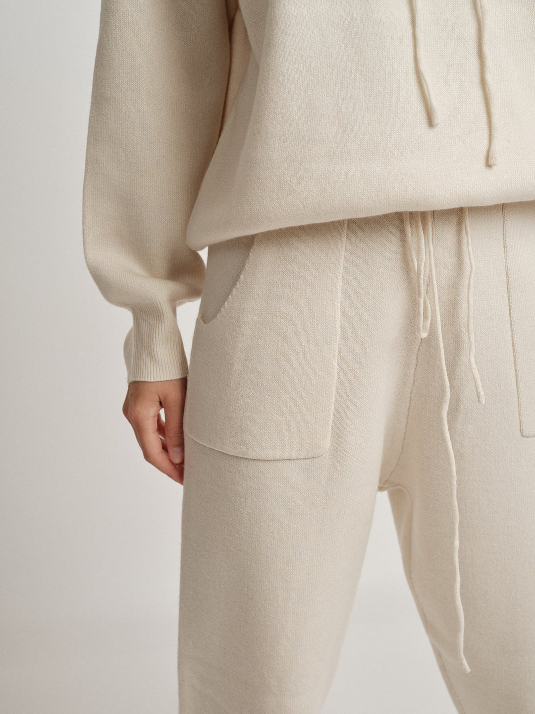Bella Cashmere Lounge Set: Detailaufnahme eines eleganten, beigen Hoodies und Joggers mit Taschen.