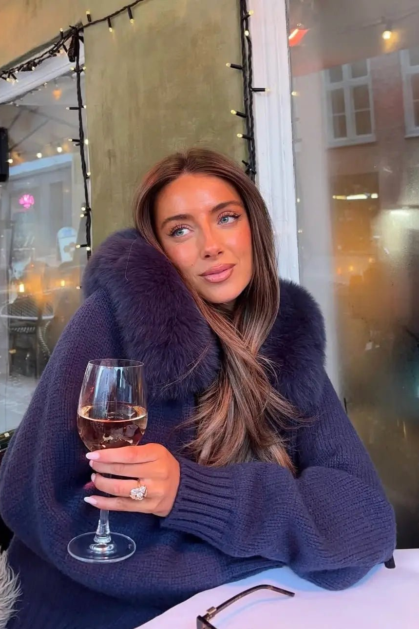 BELAMY – Chaleur Kapuzenpullover mit Fellbesatz getragen von einer Frau mit einem Glas Wein.