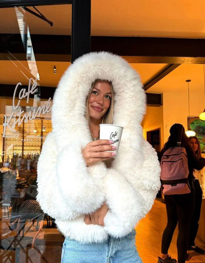 AMÉLIE  – Flauschige Felljacke mit Kapuze in einem Café, die warme Eleganz für den urbanen Lifestyle.