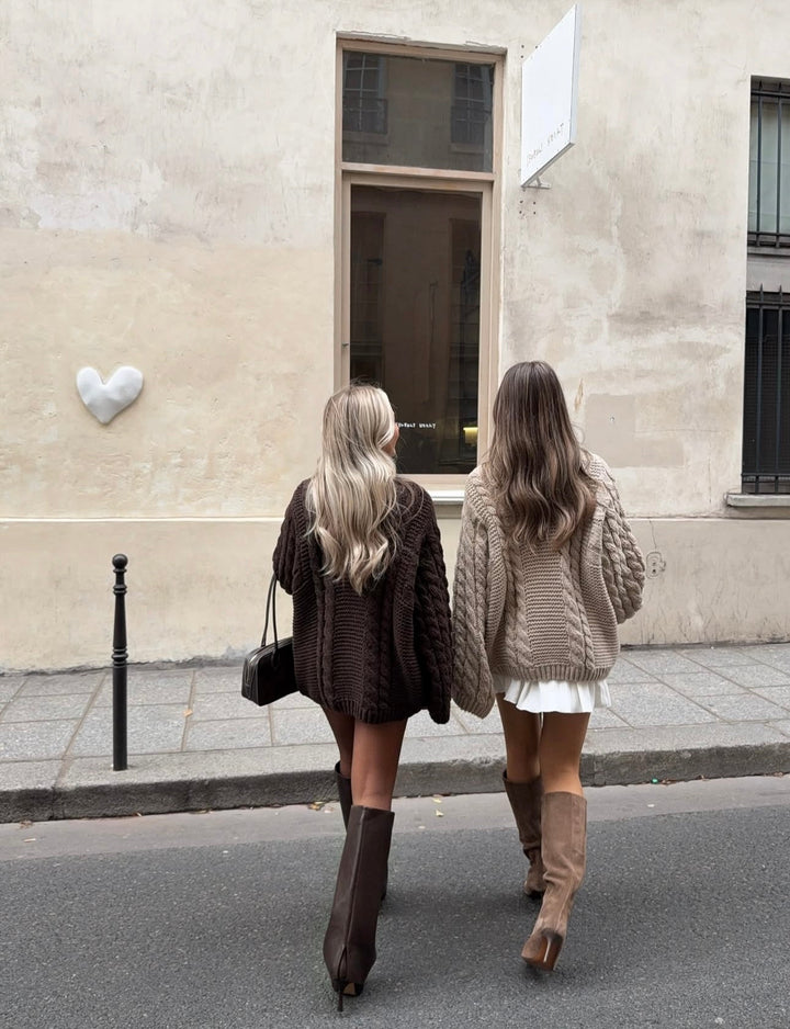 Zwei Frauen tragen den ELISE – Oversize Zopf‑Strickpullover für Damen während sie durch eine Straße in Paris gehen.