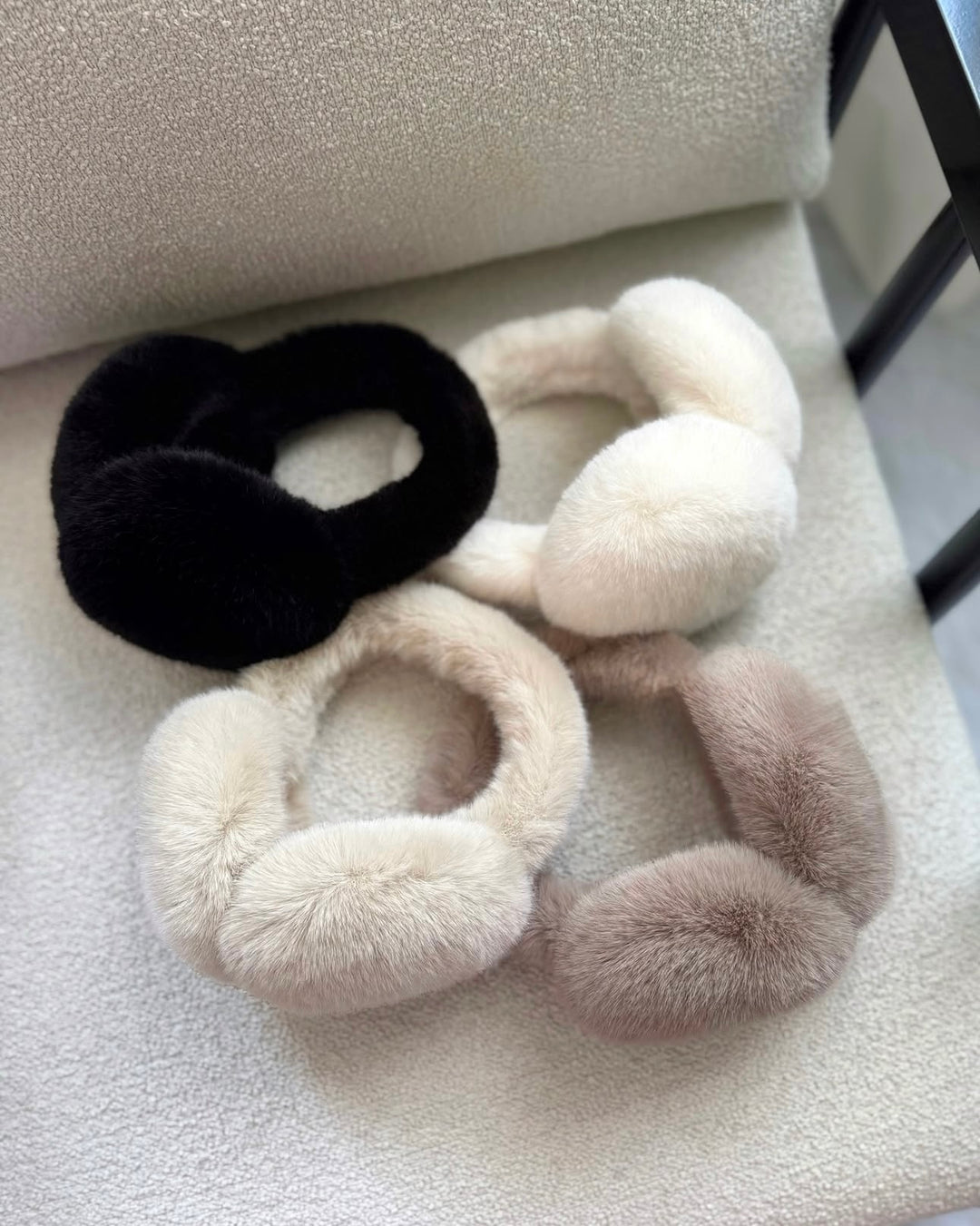 SOLEIL - flauschige Kunstpelz Ohrenwärmer in Schwarz, Weiß, Beige und Grau auf einem Stuhl.