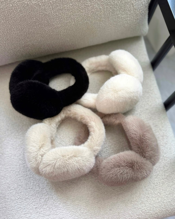 SOLEIL - flauschige Kunstpelz Ohrenwärmer in Schwarz, Weiß, Beige und Grau auf einem Stuhl.